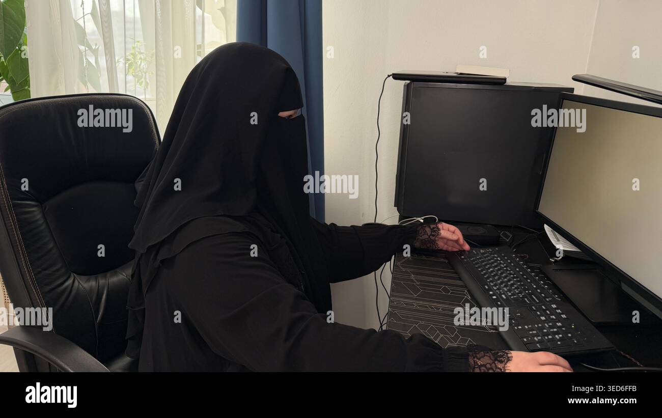 Donna che indossa un hijab che utilizza un computer desktop con un monitor bianco vuoto. Concetto di web design, UI mockup e servizi digitali. Foto Stock