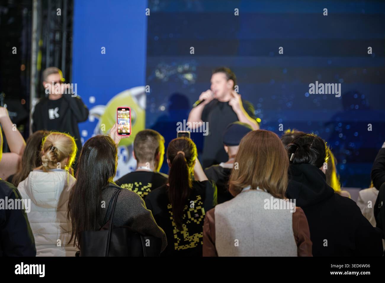 I film del pubblico esibiscono concerti dal vivo con smartphone, cantanti sul palco, luci colorate e un'atmosfera di folla vivace. Foto Stock