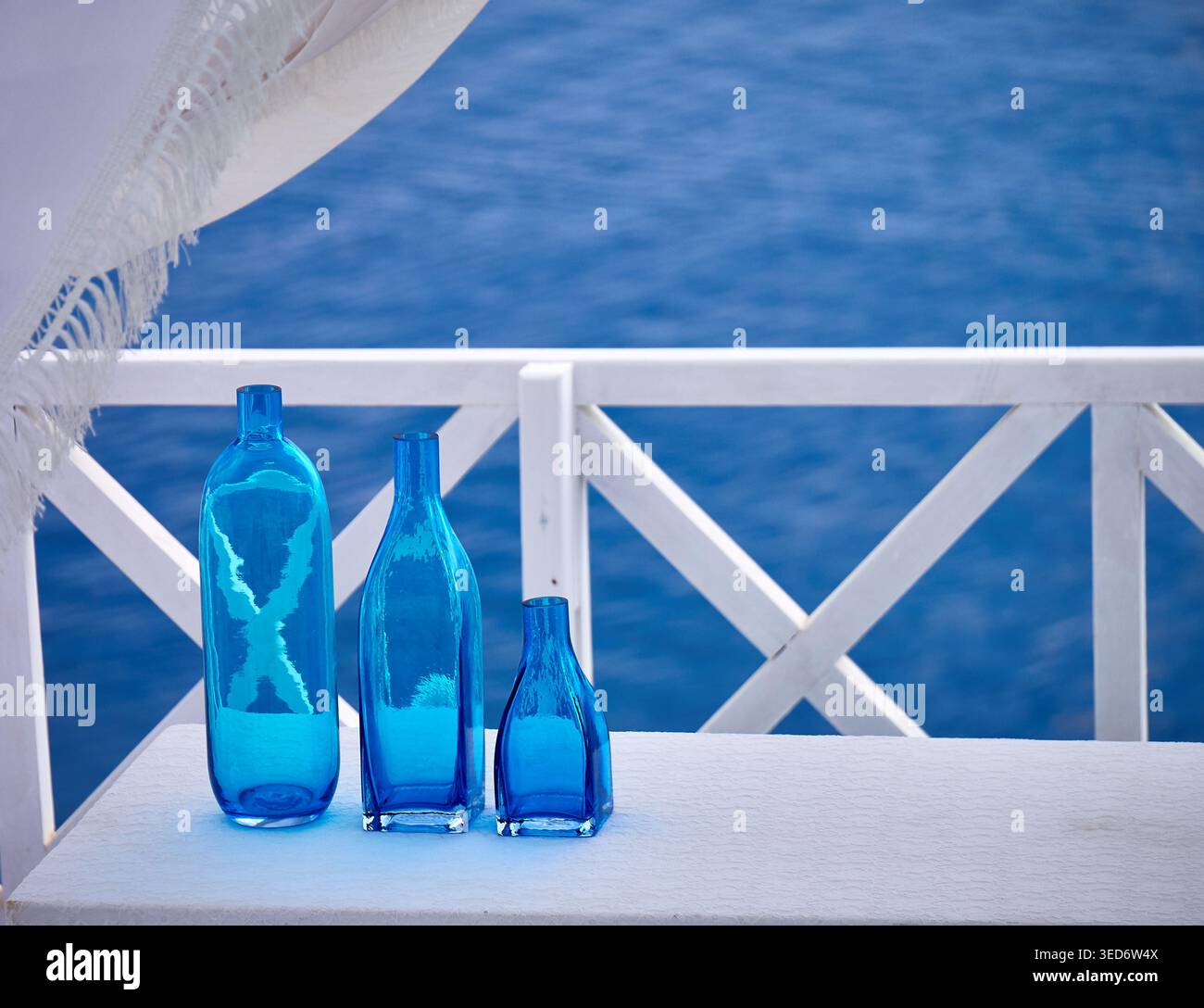 Bottiglie di vetro blu sulla terrazza bianca che si affaccia sul tranquillo Mar Mediterraneo - decor estivo costiero Foto Stock