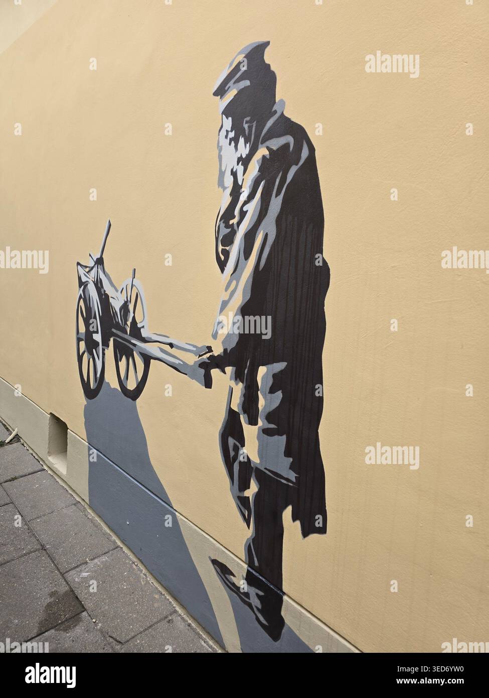 Stencil monocromatico murale di una figura in uniforme che spinge un cannone su un muro a Vilnius, Lituania - Immagine stock catturata con smartphone