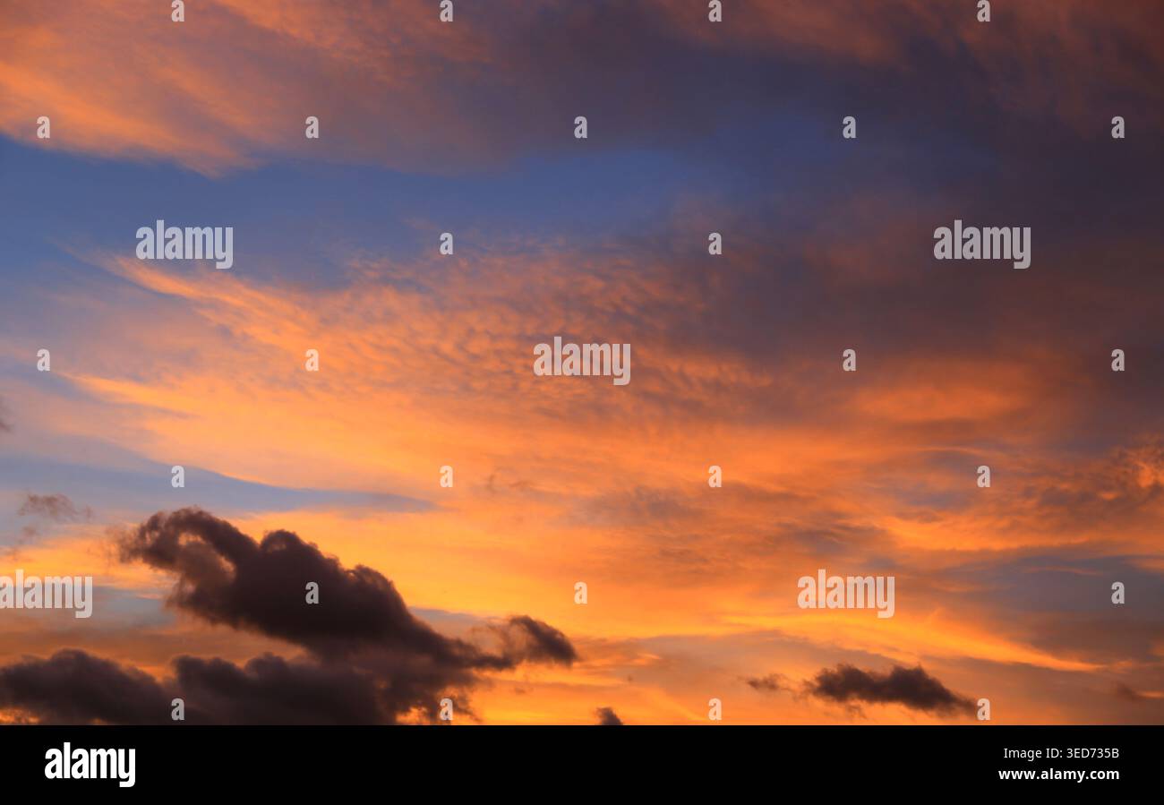 Il cielo è dipinto con sfumature ardenti di arancione e giallo mentre il sole scende sotto l'orizzonte, contrastando con il blu profondo e le nuvole scure Foto Stock