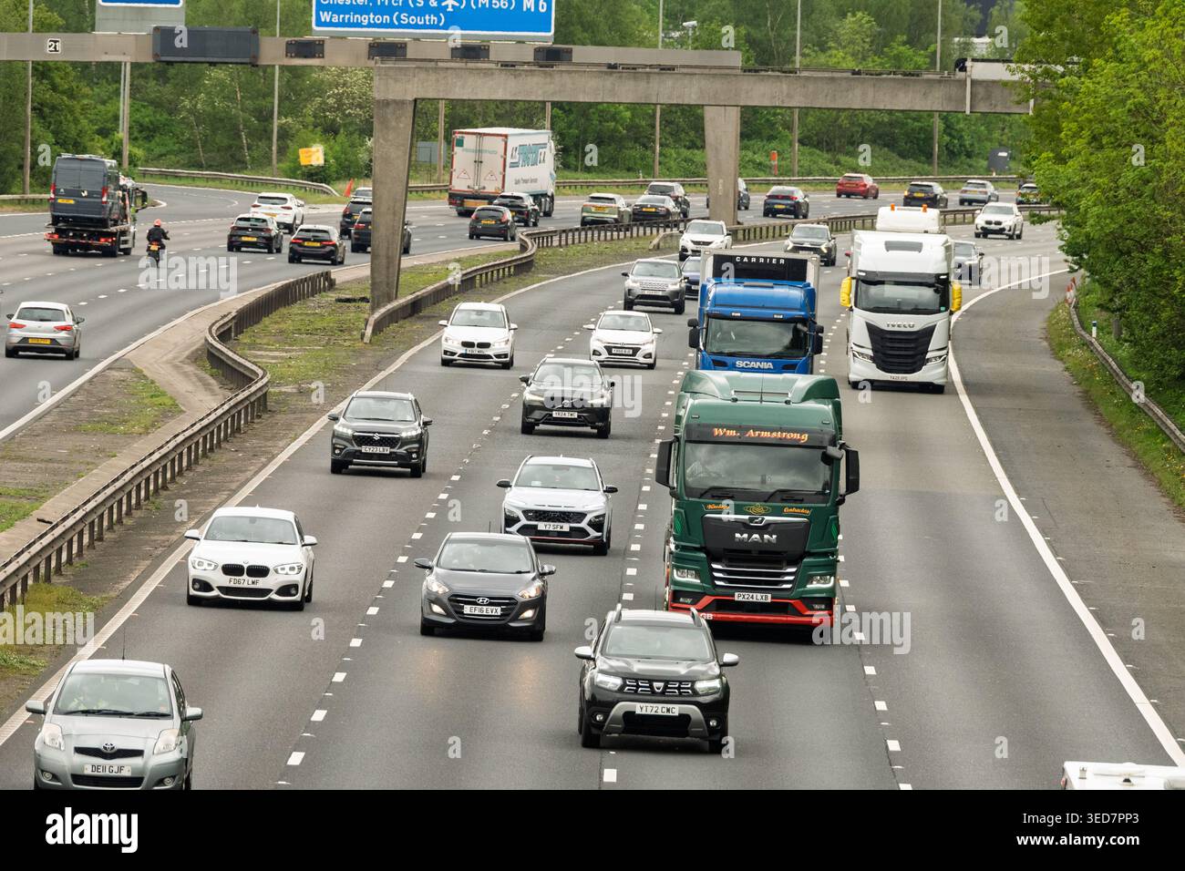 Numerosi veicoli riempiono le corsie della M6 a nord di Warrington, mostrando una tipica giornata intensa. Camion e auto navigano attraverso il verde lussureggiante circostante Foto Stock