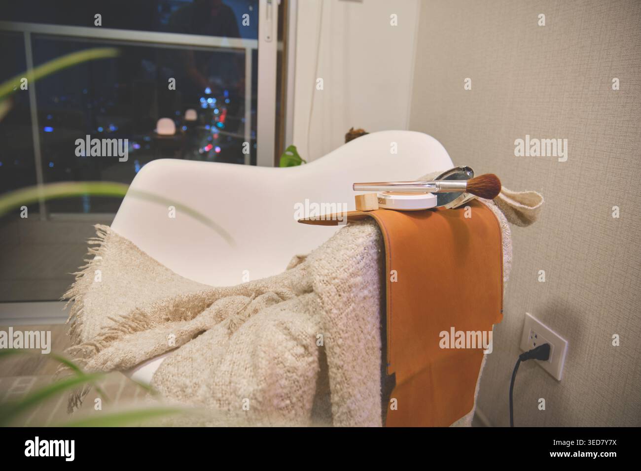 Comoda poltrona con prodotti di base per una rilassante routine di bellezza davanti alla vista della città di notte Foto Stock