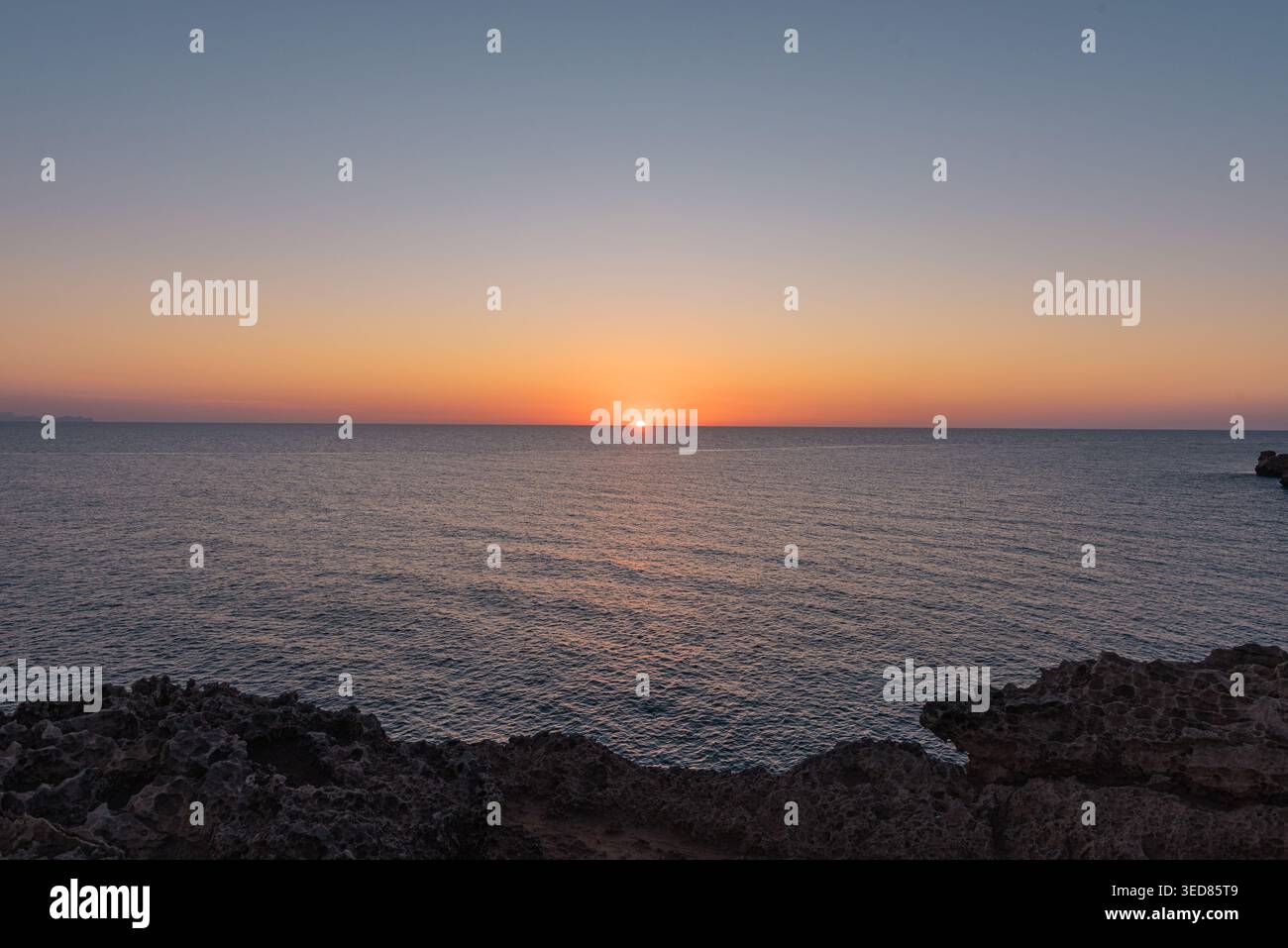 Il mare tranquillo all'alba o al tramonto, con acque serene e calme. Un cielo arancione, cieli limpidi, acque calme, rocce, uno spazio aperto, e il Mar Mediterraneo Foto Stock