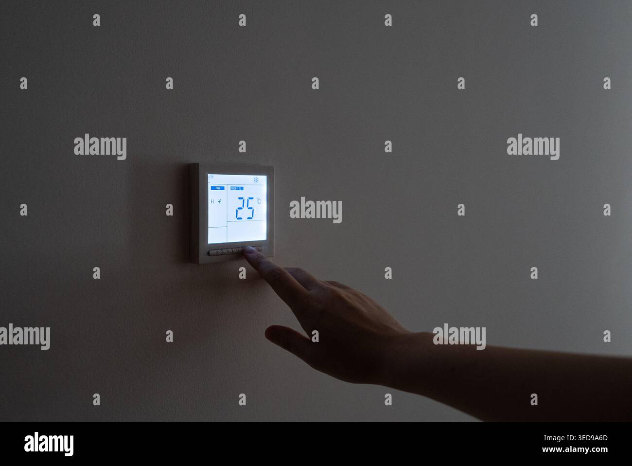 La mano di una persona posiziona un moderno termostato digitale su una parete grigia, mettendo in evidenza la tecnologia della casa intelligente, il risparmio energetico e il controllo della climatizzazione interna per lo stile di vita e l'uso aziendale. Foto Stock