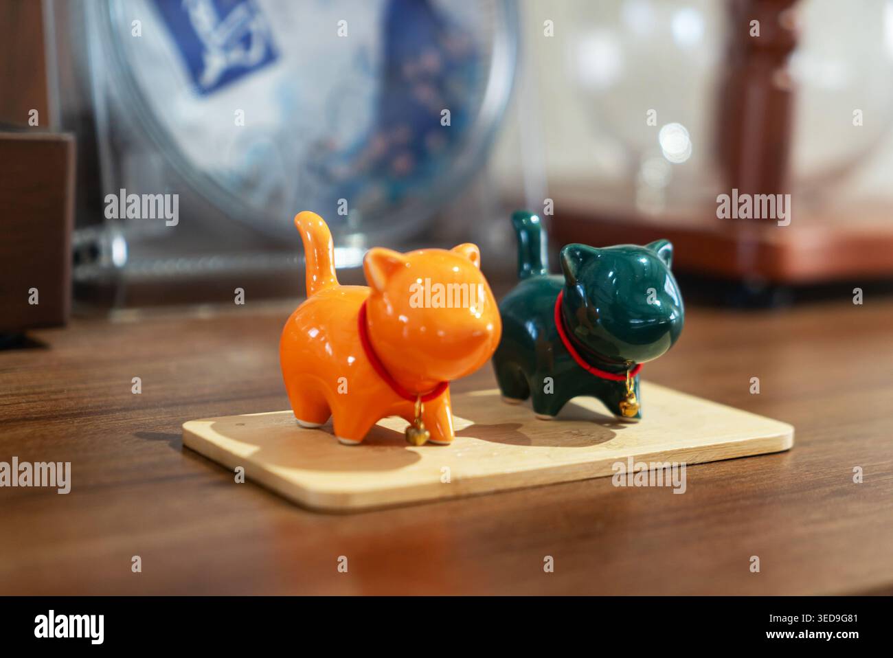Due statuette in ceramica a forma di gatto, una arancione e una verde scuro, sono esposte su una piccola tavola di legno, aggiungendo un tocco giocoso e affascinante a casa o. Foto Stock