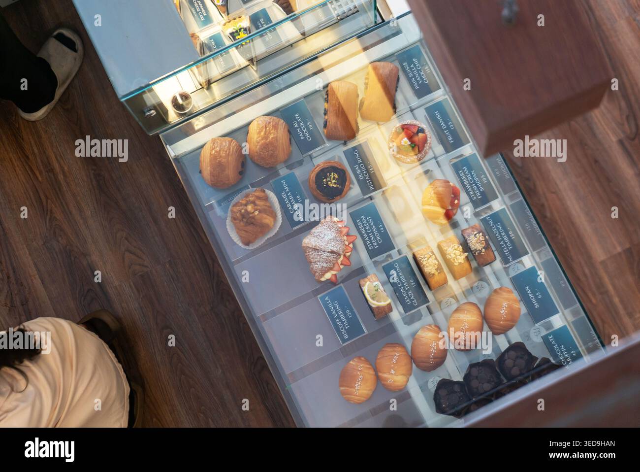 Una vetrina di vetro che mostra una varietà di dolci e dessert appena sfornati, tra cui torte, biscotti e dolci, in una moderna panetteria Foto Stock