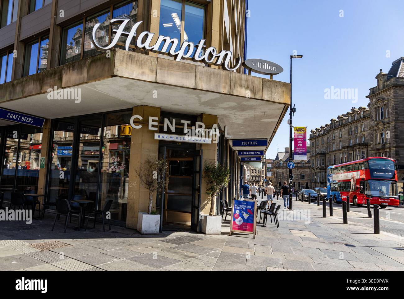 L'esterno di un hotel Hampton by Hilton e di un bar e ristorante Central in una strada soleggiata in una citta' con un autobus rosso a due piani Newcastle upon Tyne Foto Stock