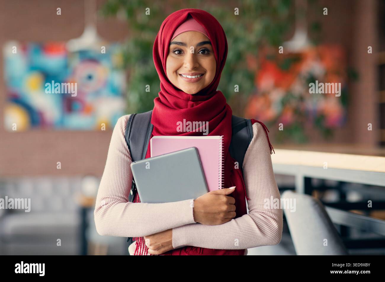 Ragazza musulmana allegra con zaino e libri al caffè Foto Stock
