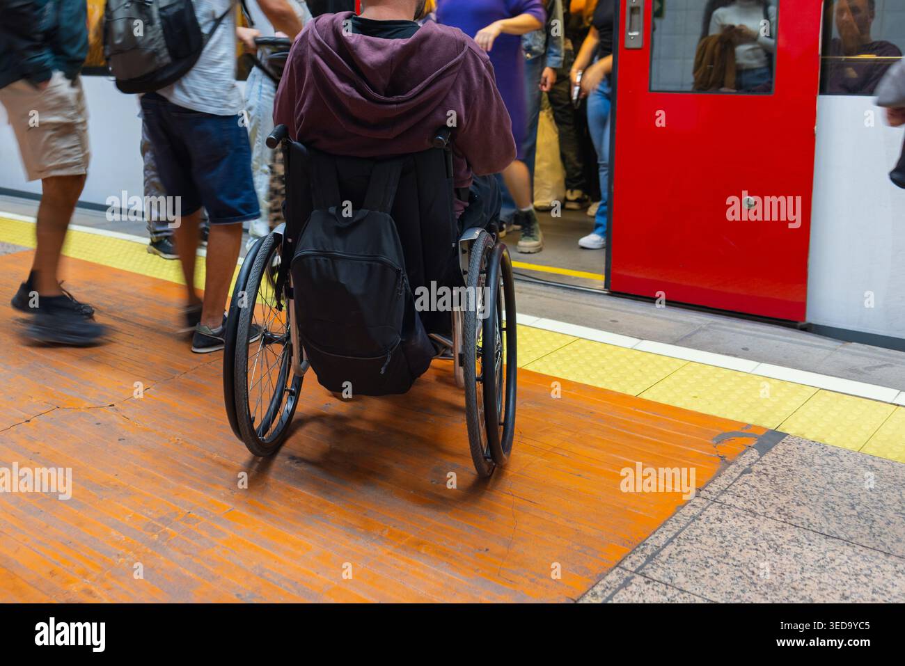 La persona con disabilità su sedia a rotelle attende mentre le persone salgono a bordo del treno della metropolitana durante gli spostamenti affollati in città. Foto Stock