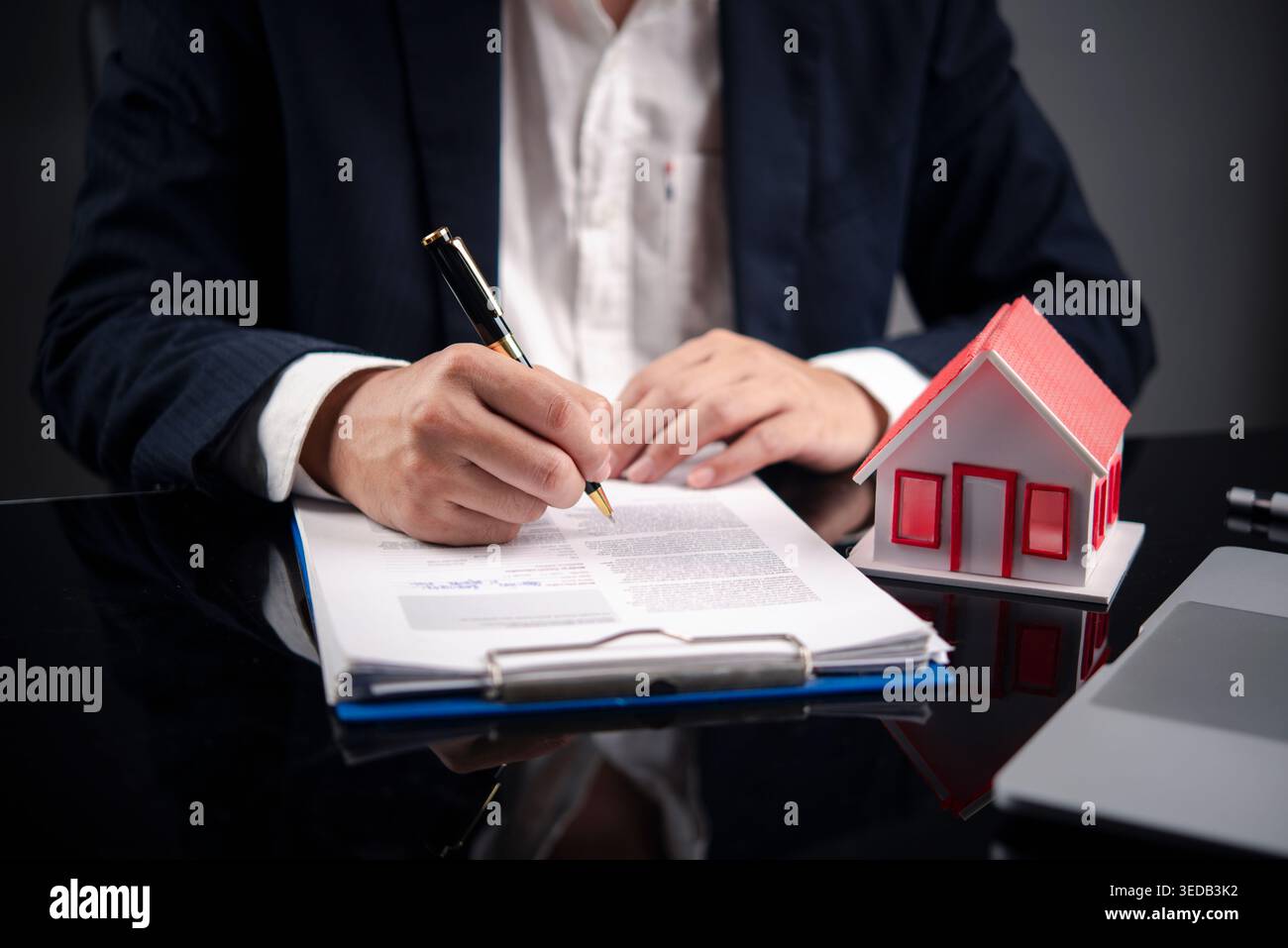 Uomo d'affari che firma un contratto per comprare casa. Uomo che firma un contratto di mutuo ipotecario con il modello di casa Red Roof. Investimenti immobiliari, insu Foto Stock
