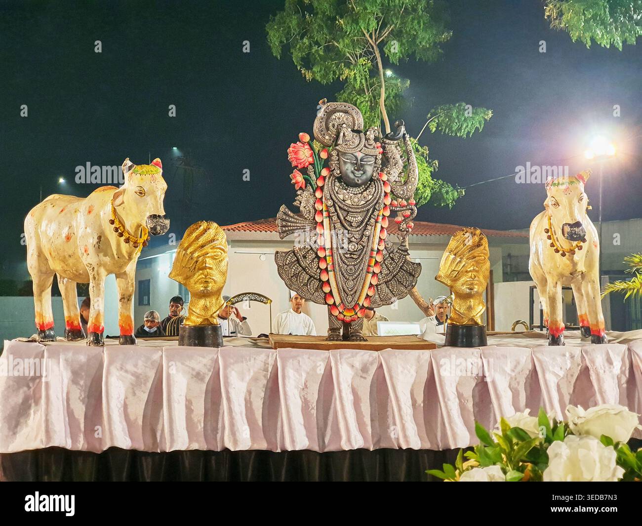 Una scena notturna all'aperto con una statua ornata di Shrinathji (una forma di Lord Krishna) posizionata centralmente su una piattaforma drappeggiata. La divinità è Foto Stock