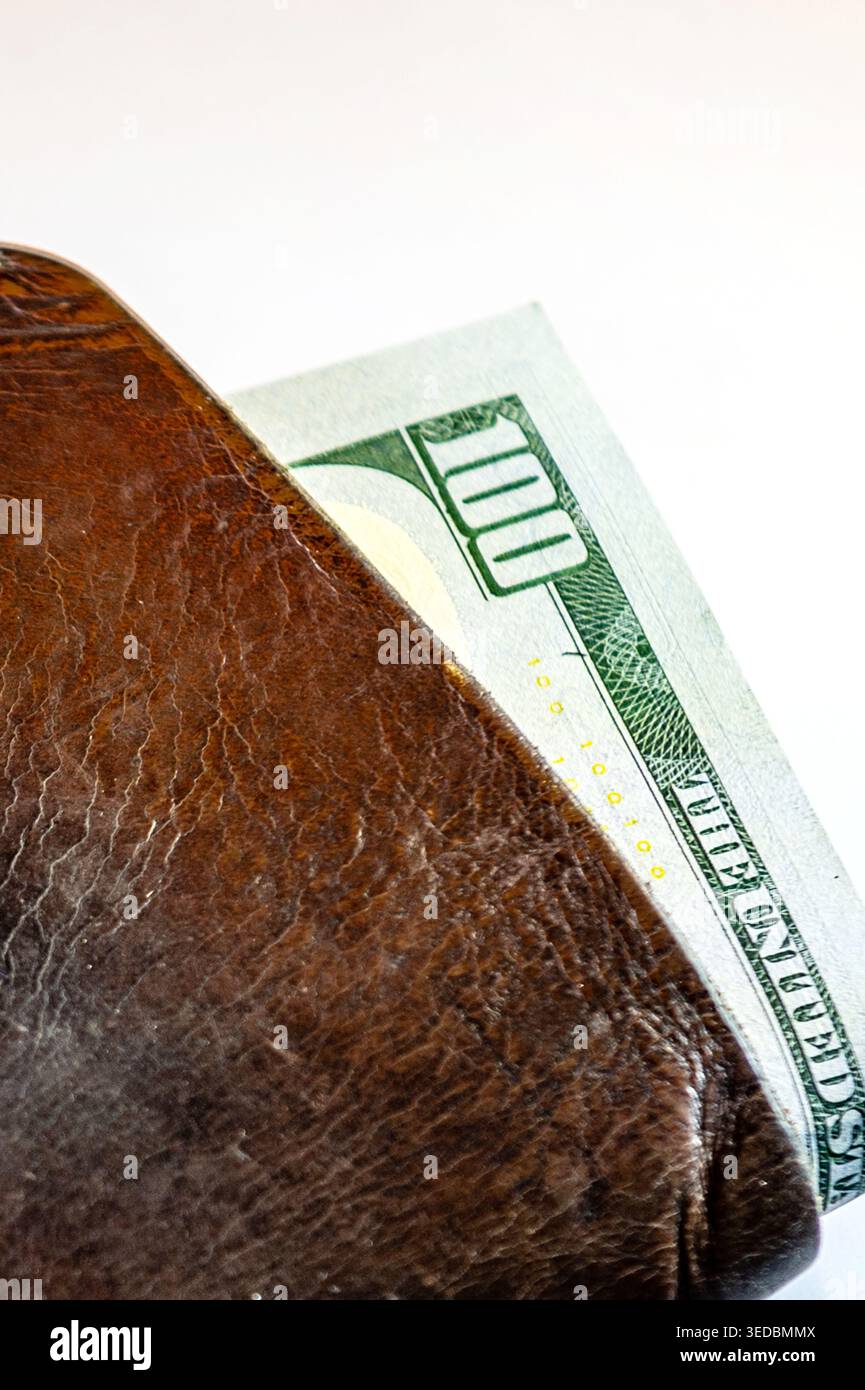Primo piano di un portafoglio marrone in pelle con banconote da cento dollari all'interno. Concetto di finanza personale, risparmio, spesa e uso quotidiano del denaro Foto Stock