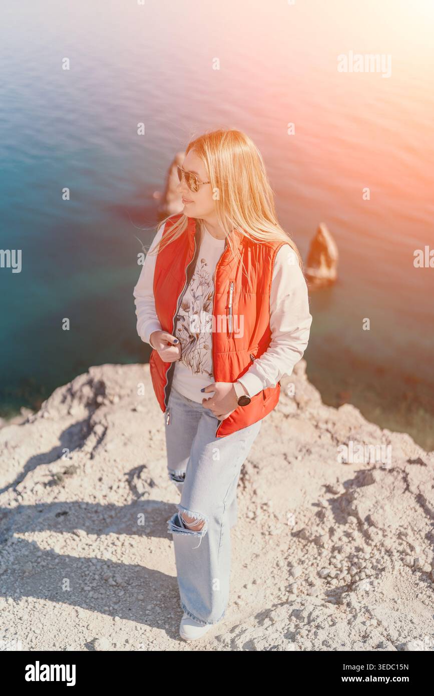 Woman Cliff Sea sorge su un bordo roccioso che si affaccia sull'acqua blu durante una vacanza di viaggio sulla costa soleggiata Foto Stock