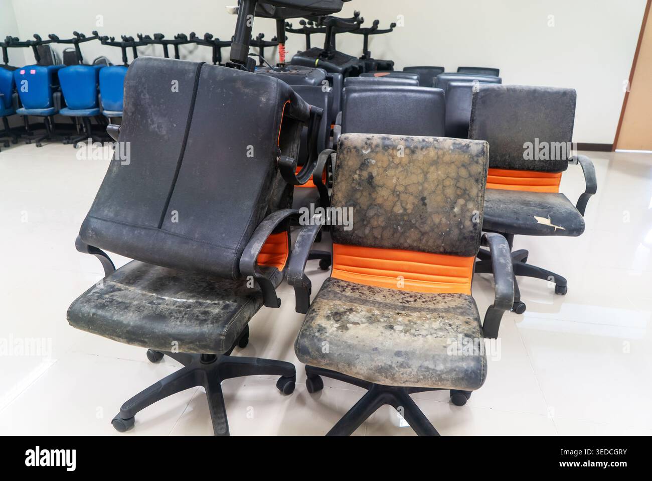 Una collezione di sedie da ufficio usurate e danneggiate in uno spazio di lavoro interno. Le sedie presentano un mix di tappezzeria nera e arancione, evidenziando l'abbandono di un Foto Stock