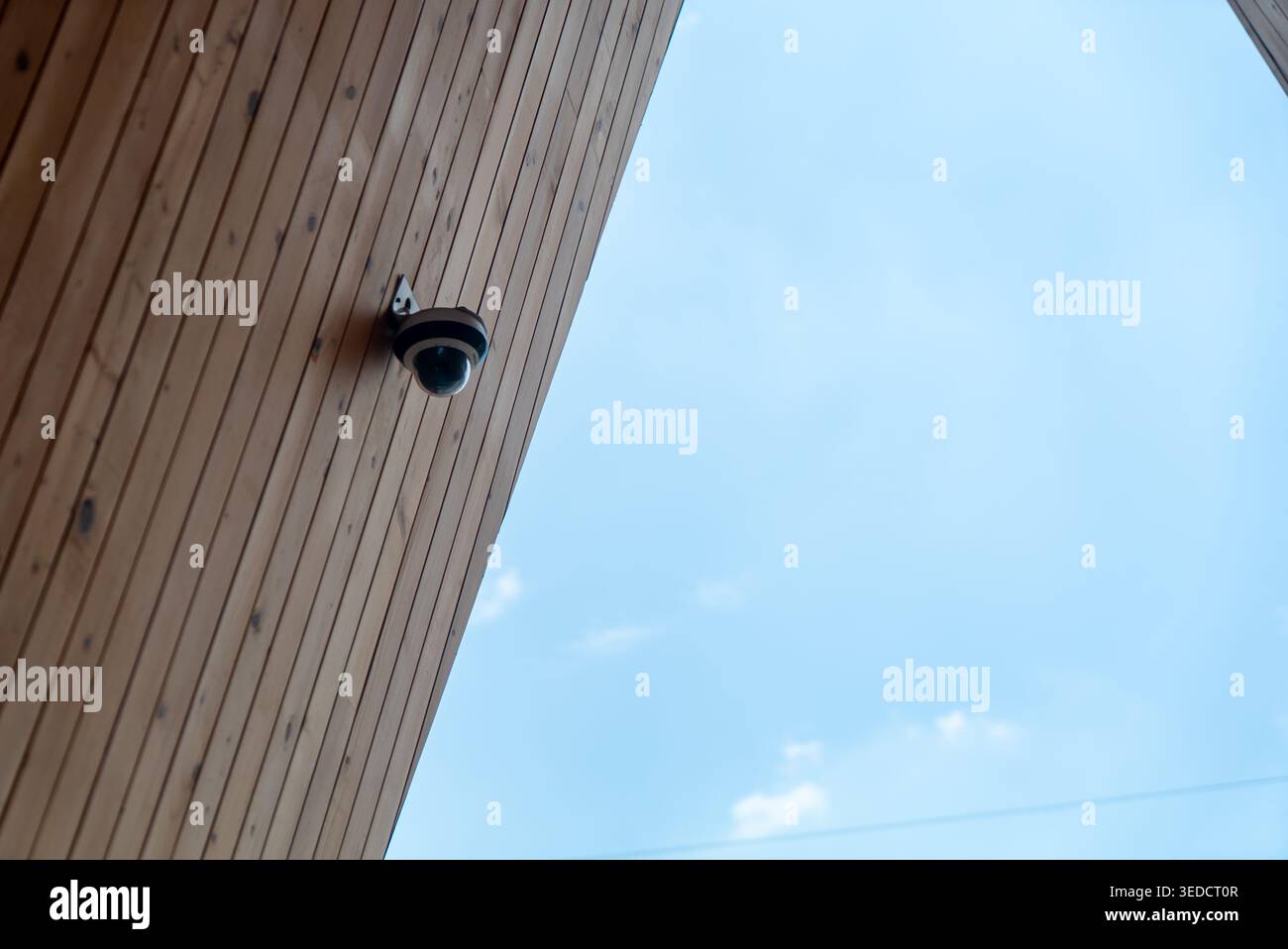 Una telecamera di sicurezza montata su una facciata in legno cattura il contrasto tra la tecnologia moderna e i materiali naturali sotto un cielo azzurro. Foto Stock
