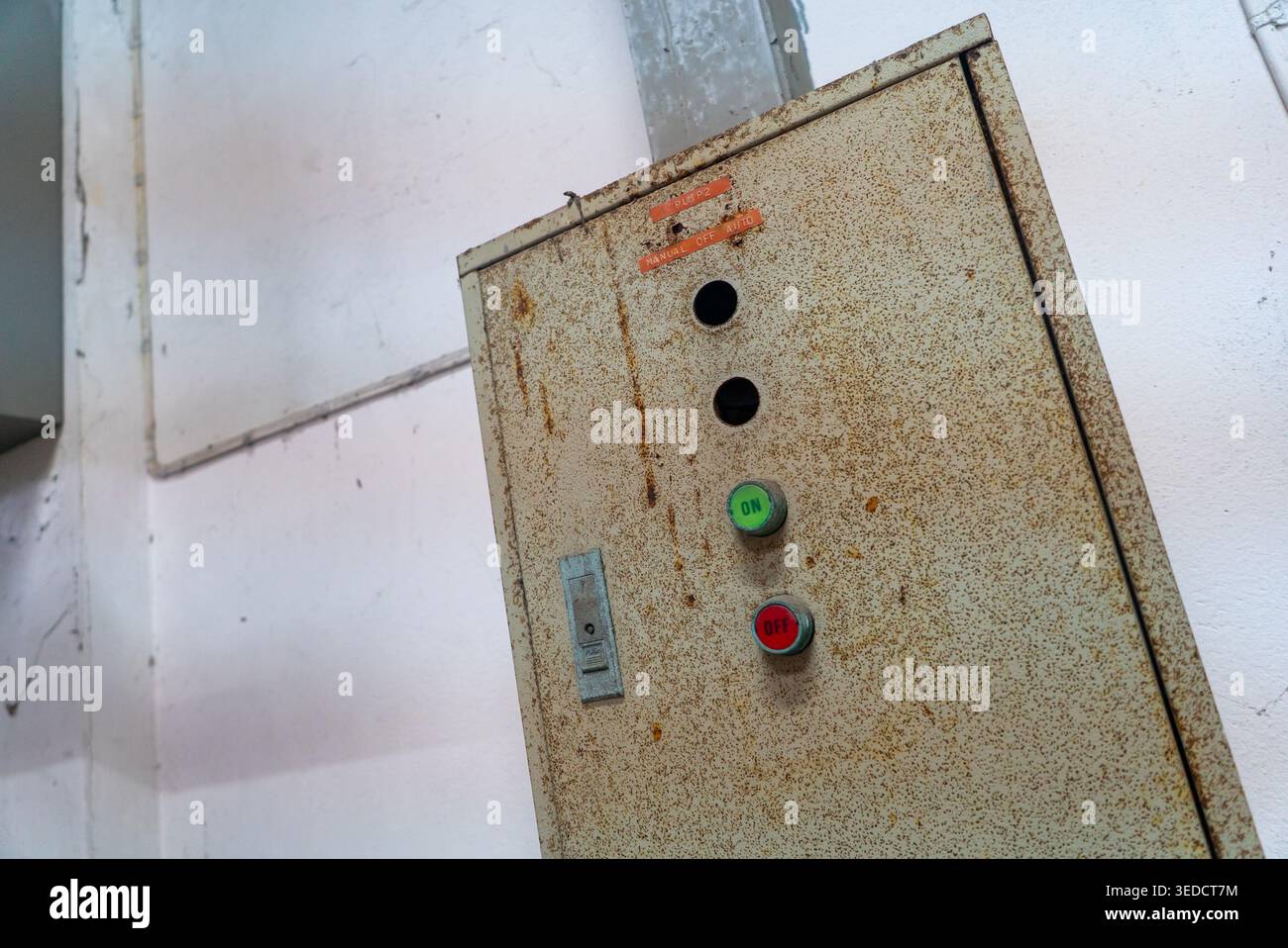 Questa immagine ravvicinata è caratterizzata da una scatola di controllo arrugginita con bottoni in un ambiente industriale sbiadito, che mostra texture in metallo invecchiato e superfici usurate, evocando Foto Stock