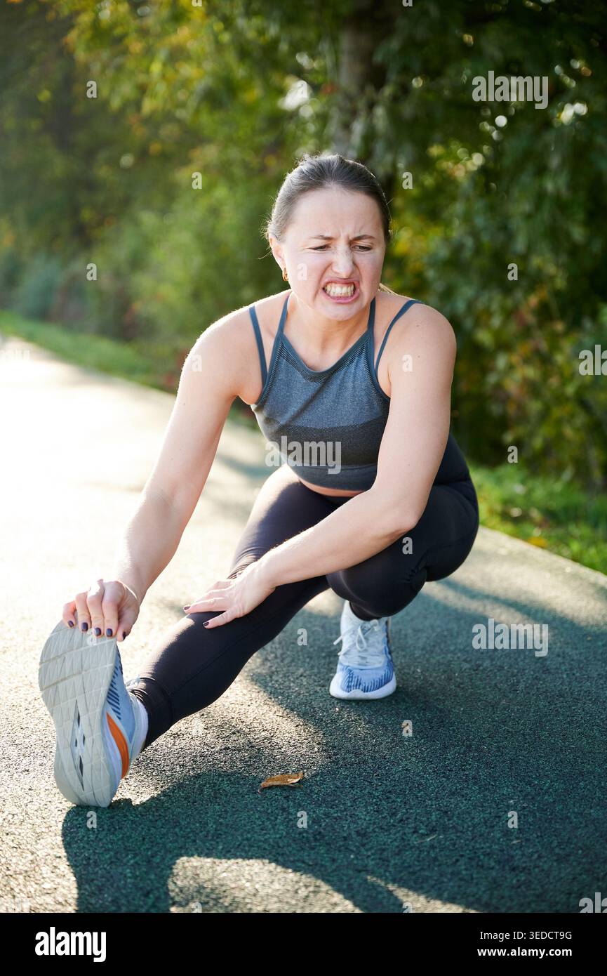 Donna che soffre mentre si allunga la gamba dopo la corsa. Donna che soffre di dolore al polpaccio sul percorso all'aperto, sforzo muscolare, lesioni, iperallenamento, problema di fitness, concetto di guarigione e salute Foto Stock