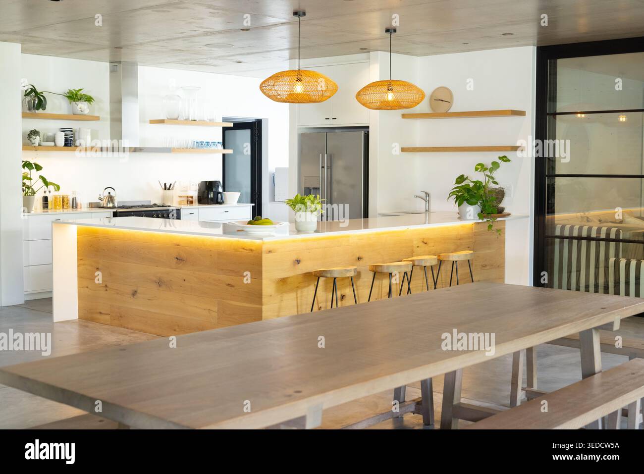Kitchen Island presenta un piano di lavoro bianco e una calda illuminazione a strisce LED, tre sgabelli e un cestino di frutta Foto Stock