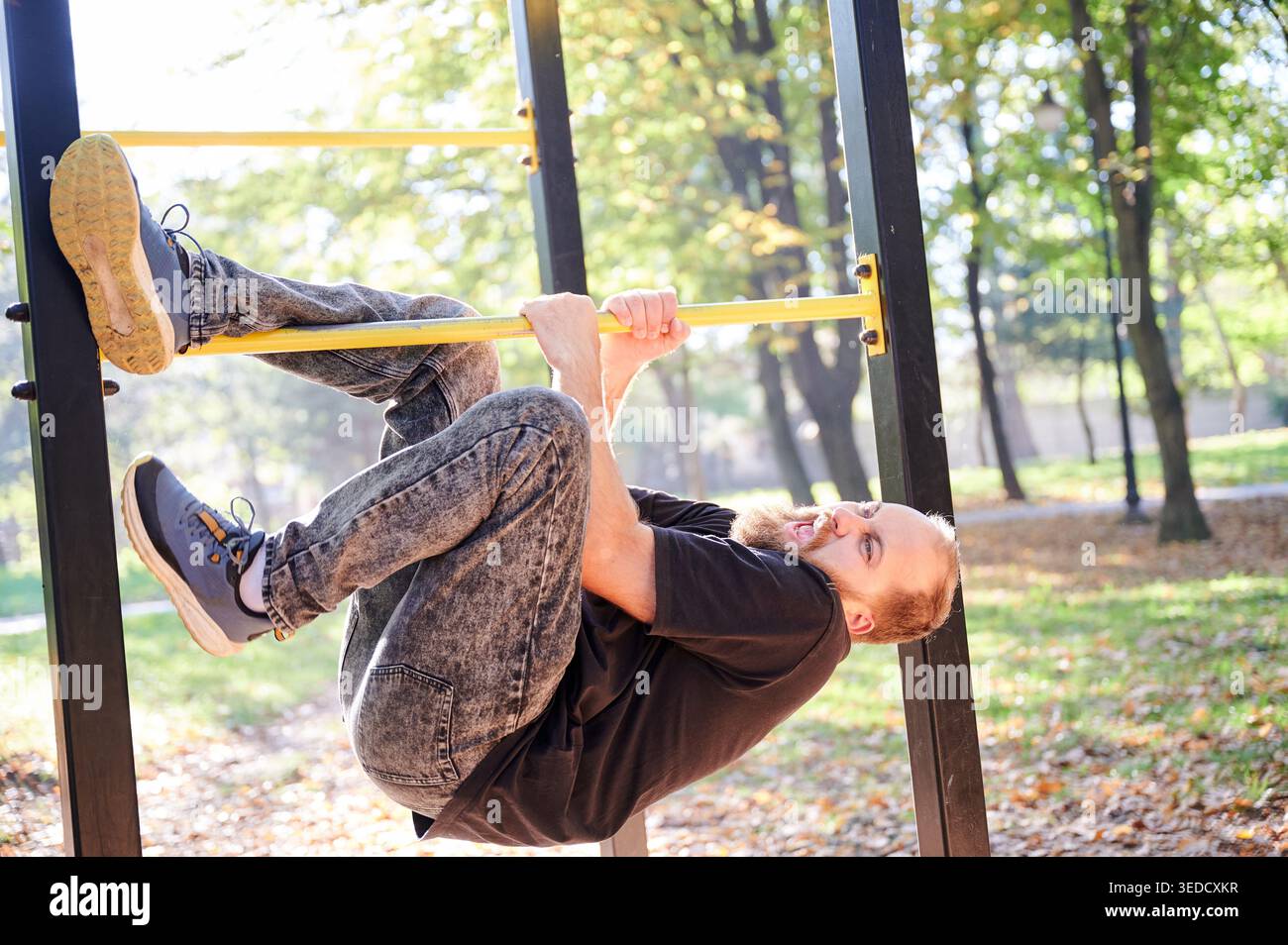 L'uomo muscolare si allena in mezzo all'autunno. Un uomo bianco determinato esegue il pullup con un'intensità focalizzata all'esterno. L'uomo con la barba e le fortezze esegue il pullup su una barra gialla durante l'autunno nel parco Foto Stock