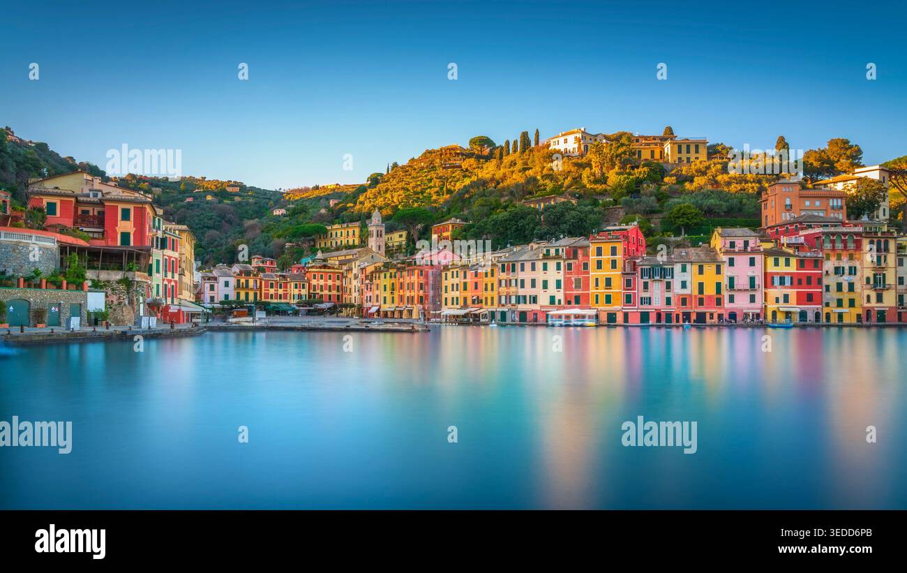 Vista a lunga esposizione dell'iconico porto di Portofino al tramonto, in Liguria. Riflessi d'acqua setosa di case colorate e luce dorata sulle colline. ITA Foto Stock