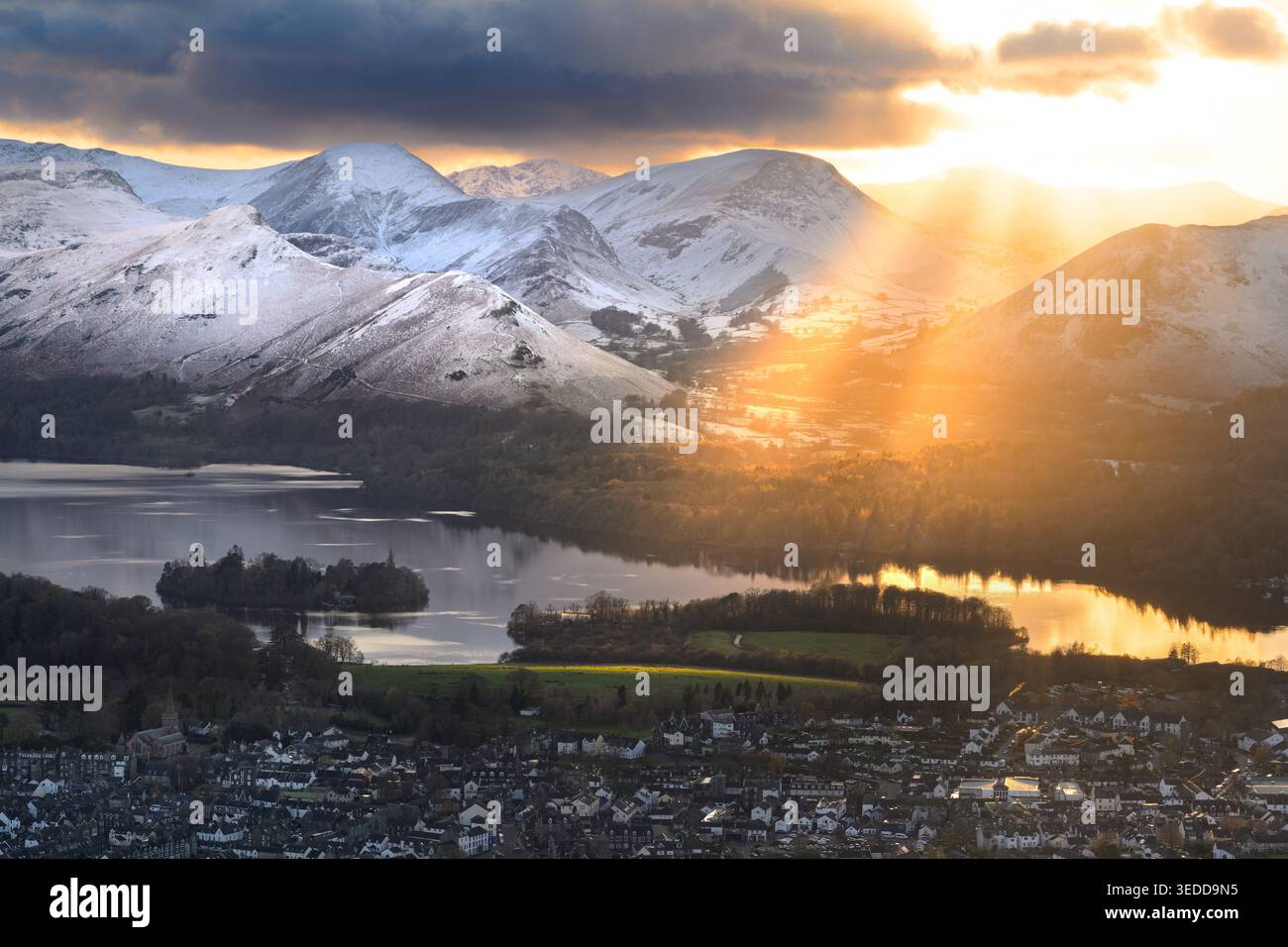 I raggi dorati del sole splendono sulle spettacolari montagne innevate che circondano Derwentwater nel Lake District National Park, Regno Unito. Foto Stock