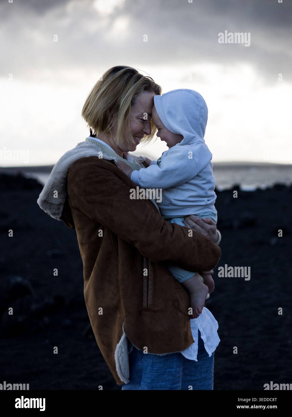 Autentico momento d'amore e di connessione tra madre e bambino vicino al mare Foto Stock