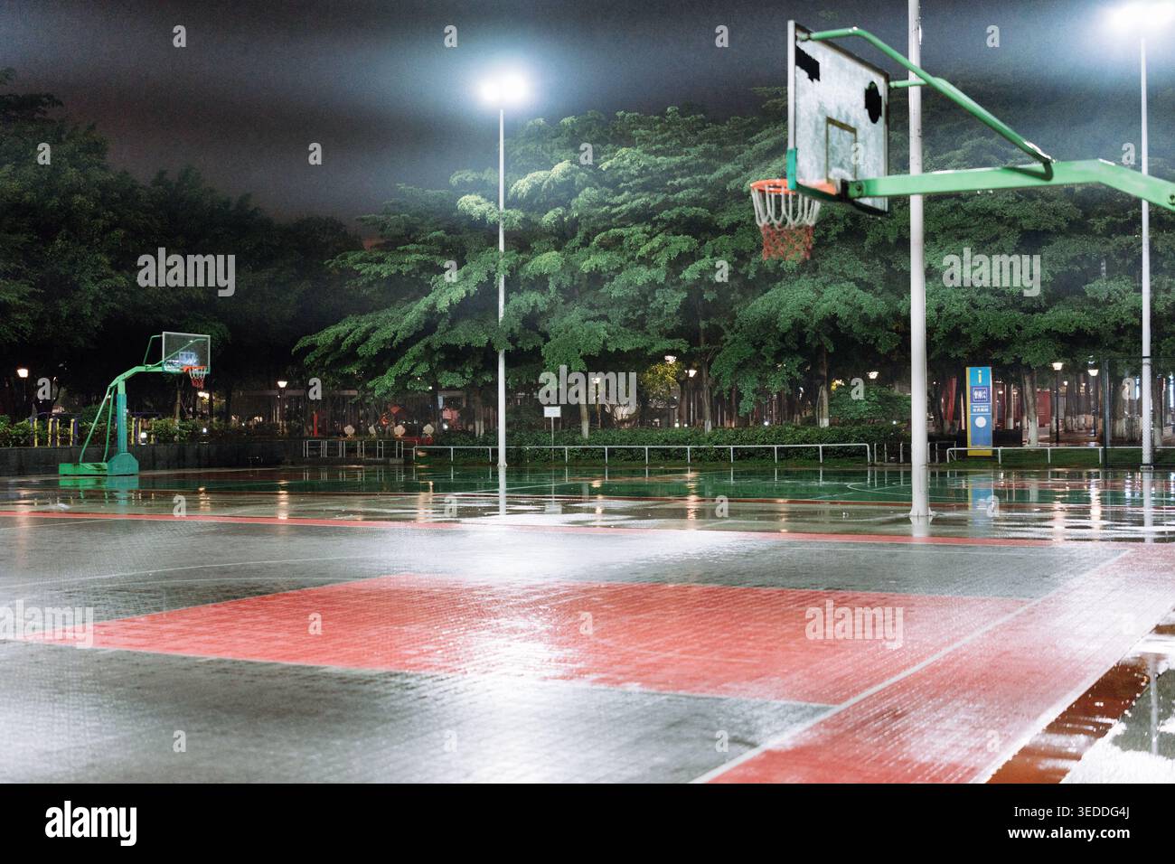 Campo da pallacanestro bagnato di notte con cerchi illuminati e luci riflettenti sulla superficie Foto Stock