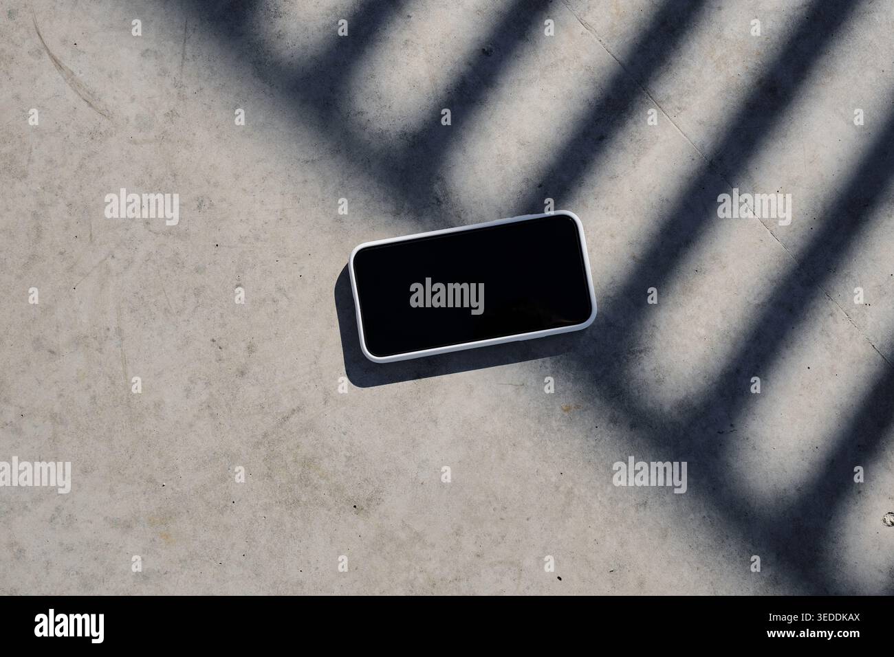 Custodia bianca per smartphone su superfici in cemento con ombre geometriche Foto Stock