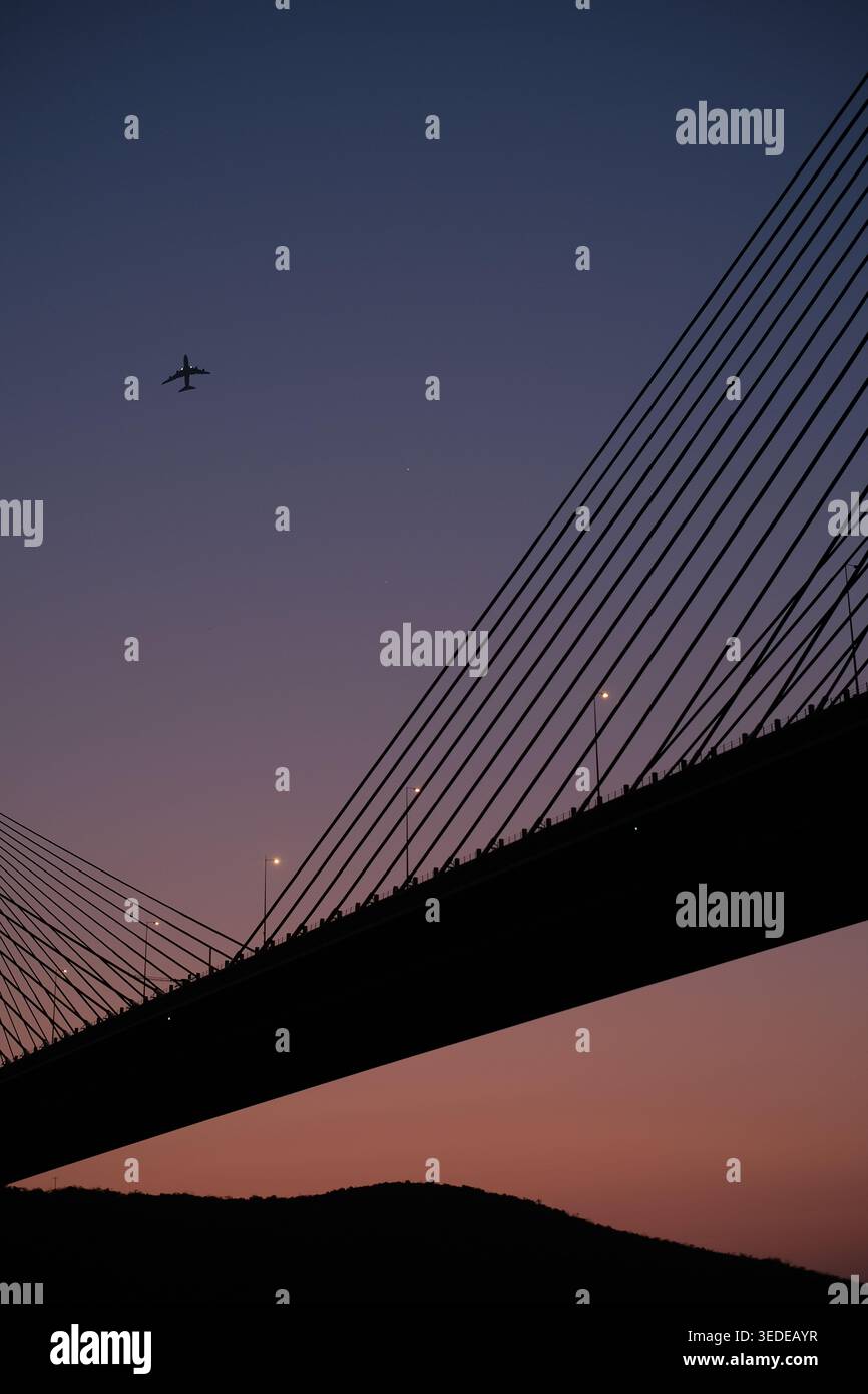 Sagoma del ponte Ting Kau contro un cielo di tramonto, con un aereo che vola sopra la testa a Hong Kong, Cina Foto Stock