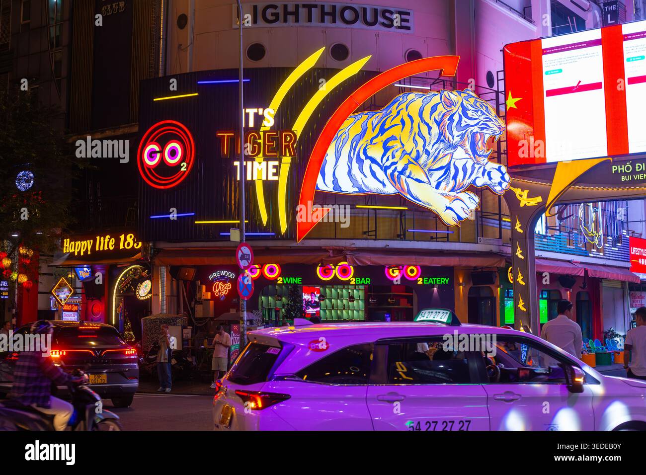 Una strada vivace di notte presenta insegne al neon, una grafica tigre ed edifici illuminati. Vita notturna della città, scena urbana, luci al neon. Vietnam, ho chi min Foto Stock
