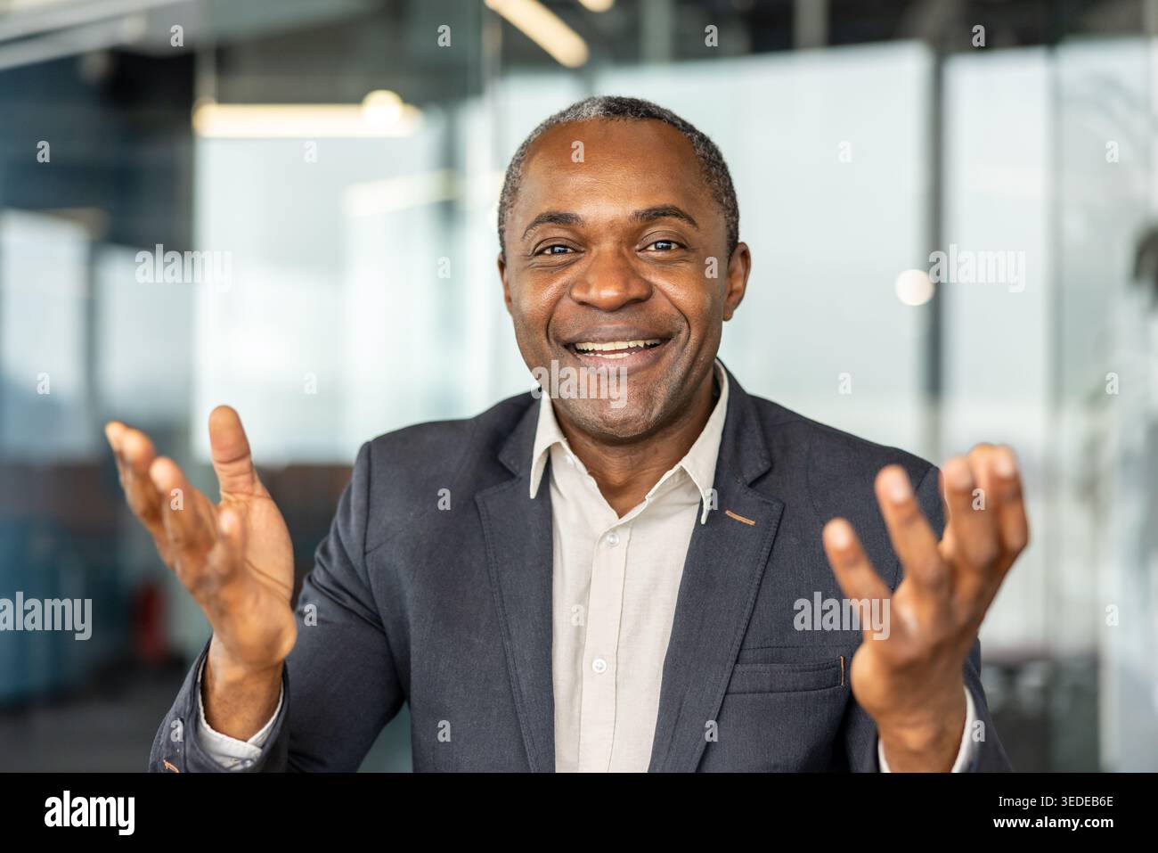 Simpatico uomo afroamericano professionista in costume sorridente e gestante con le mani aperte, che trasmette fiducia, impegno e leadership positiva in un ambiente d'ufficio Foto Stock