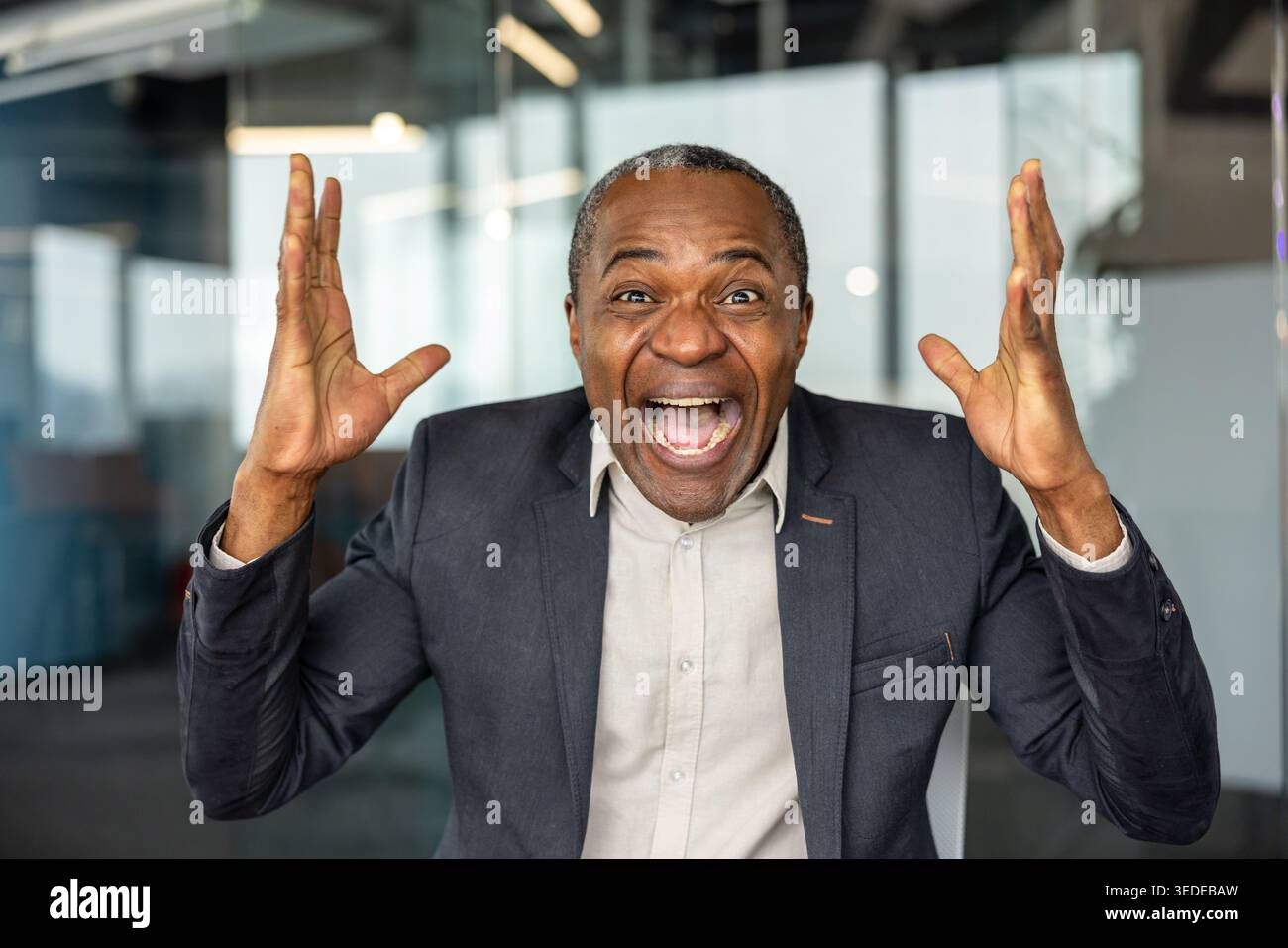 Uomo d'affari maturo che prova gioia e trionfo, festeggia felicemente un risultato significativo o raggiunge un obiettivo aziendale, esprimendo al contempo forti emozioni positive in un ambiente di ufficio Foto Stock