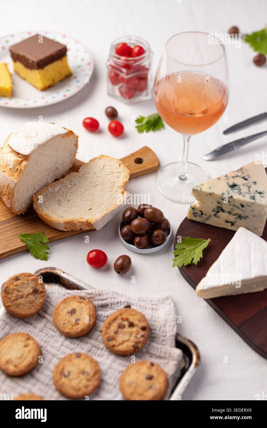 Su un tavolo ci sono fette di pane, diversi tipi di formaggio, biscotti, una bevanda e piccoli pomodori. Questa scena mostra un incontro di cibo con vari Foto Stock