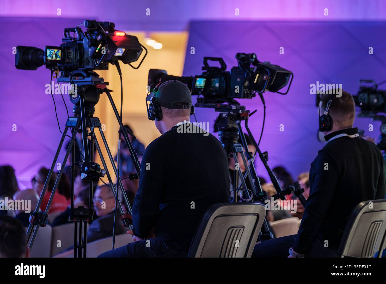 Operatori di videocamere professionali che acquisiscono eventi dal vivo con videocamere broadcast, cuffie, cavalletti e illuminazione viola del palcoscenico. Foto Stock