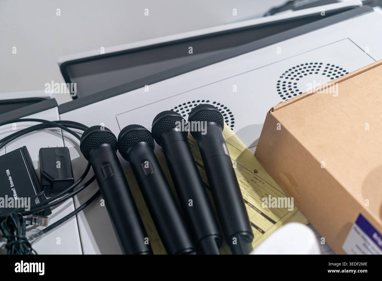 Una collezione di microfoni neri disposti su una superficie bianca, circondati da apparecchiature audio e cavi, perfetti per la registrazione del suono e la performa dal vivo Foto Stock