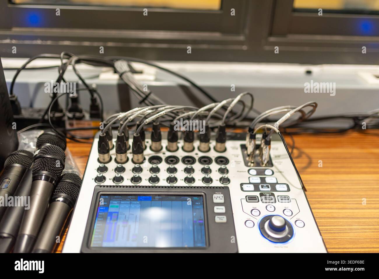 Una visione dettagliata di un mixer audio circondato da microfoni e cavi, che mette in mostra tecnologie sofisticate per la registrazione audio e le prestazioni dal vivo. Foto Stock
