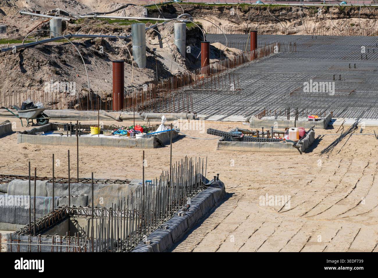 Vista dettagliata di un cantiere con preparazione della sabbia, rete di rinforzo in acciaio e utensili pronti per il versamento di fondazioni in calcestruzzo e lavori di pavimentazione Foto Stock