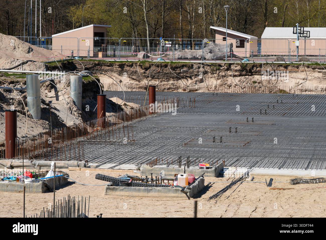 Ampia visuale di un cantiere che mostra la rete di rinforzo in acciaio posata per fondamenta in calcestruzzo, con scavi, tubi e attrezzature visibili Foto Stock