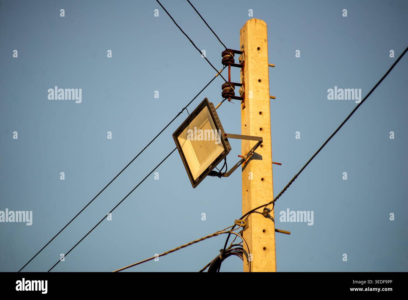 Un'asta di servizio è dotata di un proiettore montato lateralmente, circondato da linee elettriche contro un cielo azzurro, che mette in luce la moderna luce per esterni Foto Stock
