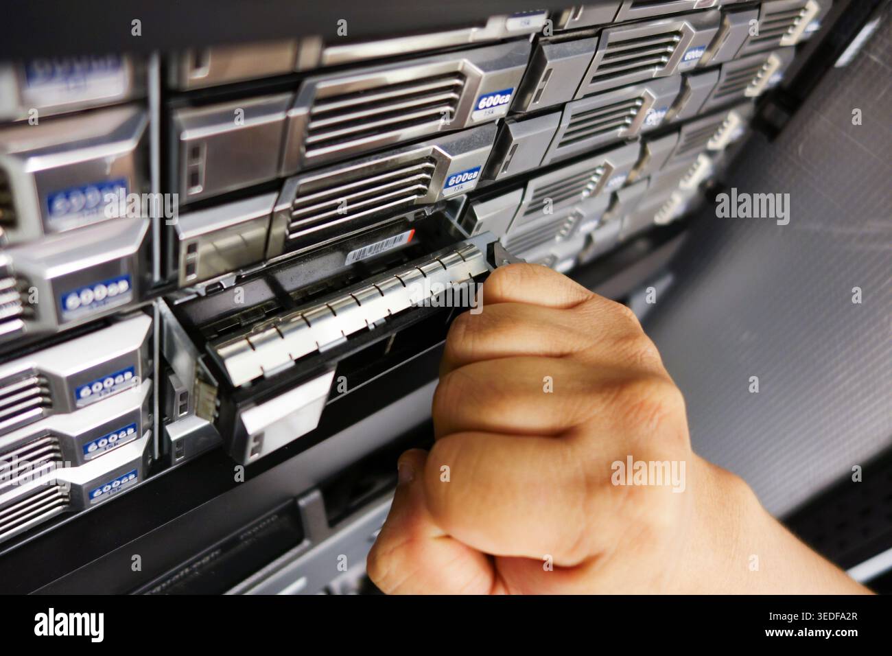 Primo piano di una mano che inserisce un modulo dati in un rack server, illustrando le complessità della gestione hardware e delle operazioni tecnologiche in DIGI Foto Stock
