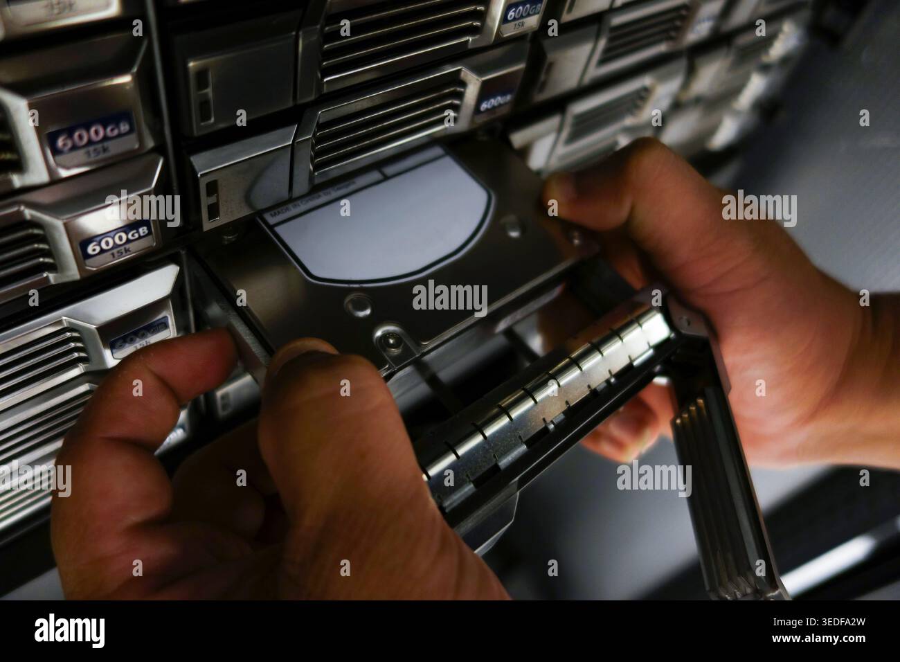 Una visione ravvicinata delle mani che gestiscono con attenzione un dispositivo di memorizzazione dati all'interno di un server rack, che mostra l'intricata tecnologia coinvolta nella gestione dei dati Foto Stock