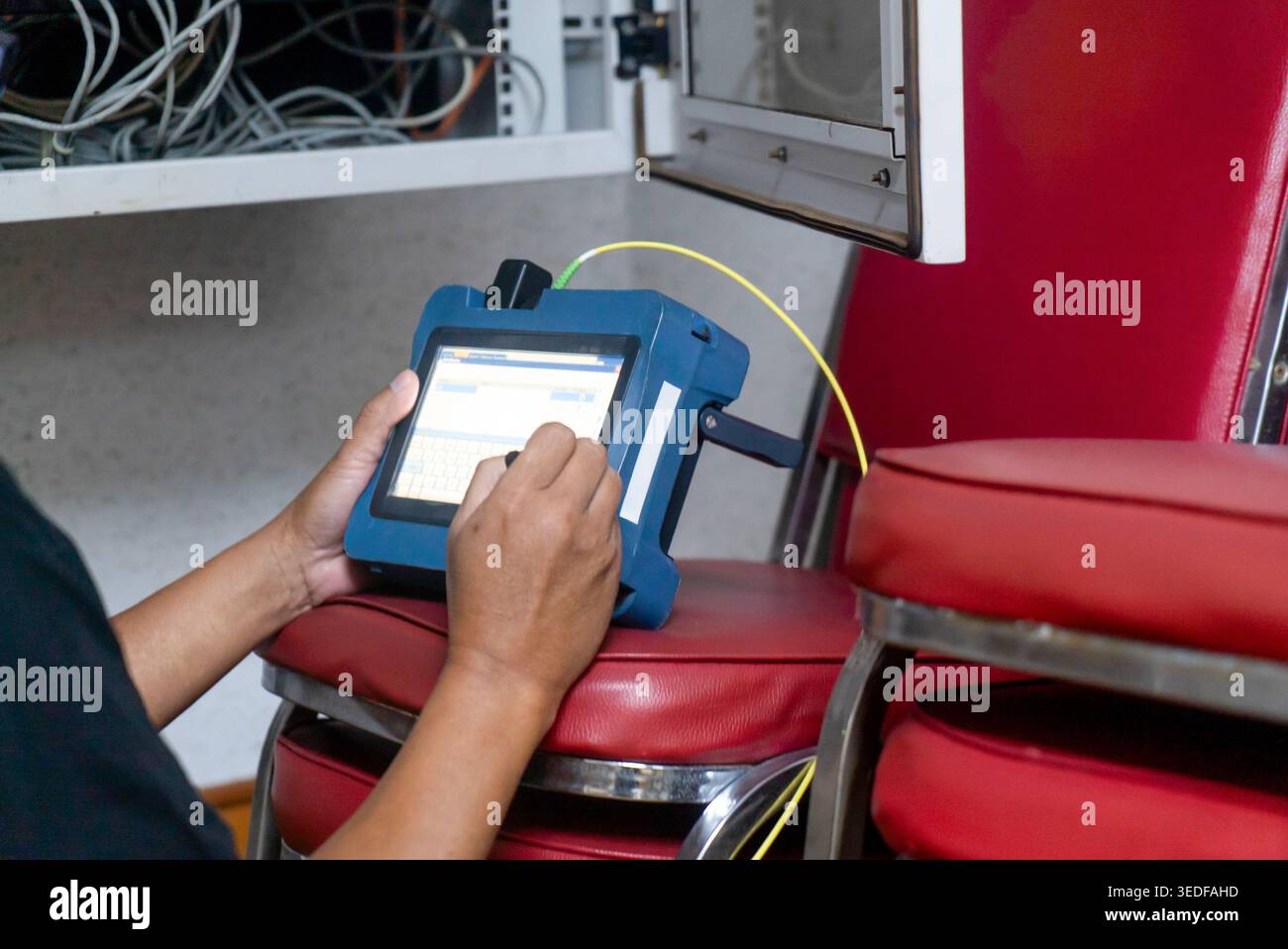 Un tecnico utilizza un dispositivo di test portatile in un'officina, mostrando l'interazione con la tecnologia e gli strumenti per l'analisi dei dati e la diagnostica. Foto Stock