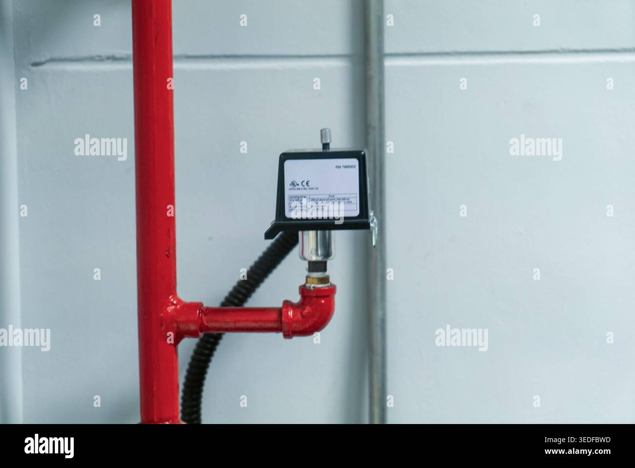 Primo piano di un tubo rosso dotato di manometro in un ambiente industriale, che mostra le apparecchiature critiche per il monitoraggio e il controllo dei fluidi flo Foto Stock