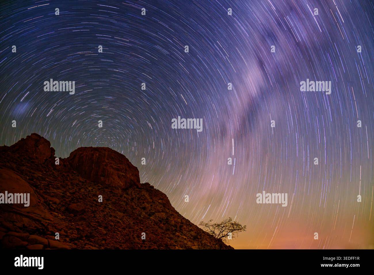 Sentieri stellari su Inselberg di granito Spitzkoppe, Namibia, cielo notturno a lunga esposizione, rotazione circolare delle stelle, via Lattea, profilo di alberi solitari, terre desertiche Foto Stock