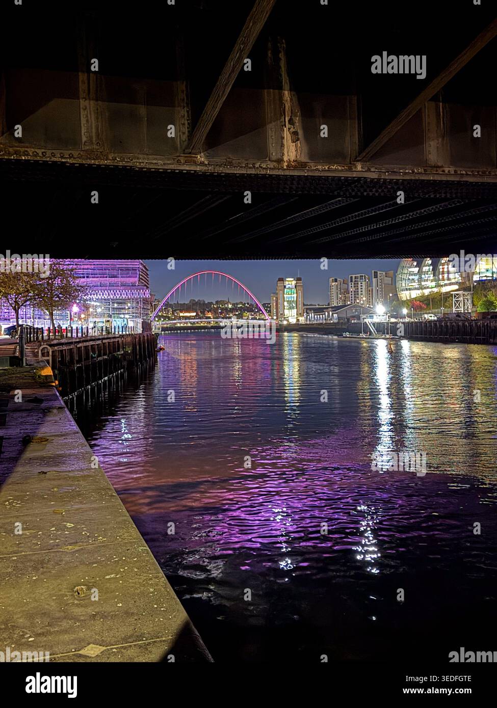 Vista notturna del Millennium Bridge che attraversa il fiume Tyne a Newcastle upon Tyne con vivaci luci viola della città riflesse nell'acqua Foto Stock