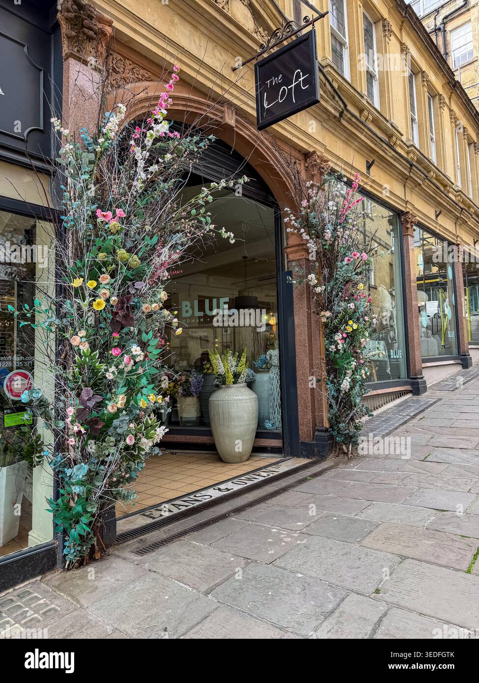 Un affascinante punto vendita, l'entrata del Loft, decorata con elaborate composizioni floreali in alti vasi su una strada acciottolata nella storica città di Bath Foto Stock