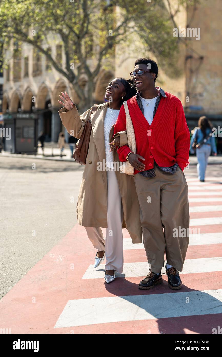 Amici afro-americani spensierati, uomo e donna camminano lungo l'incrocio ridendo e parlando. Foto Stock