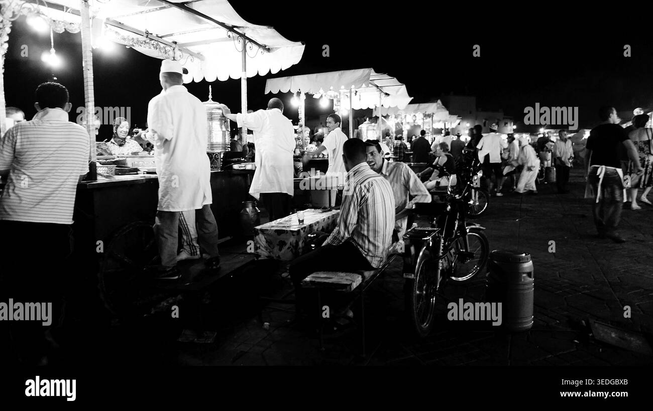 Persone alle bancarelle di cibo in un vivace mercato notturno, shot in bianco e nero, bancarelle di cibo serali a Djemaa el Fna, Marrakech, Marocco Foto Stock