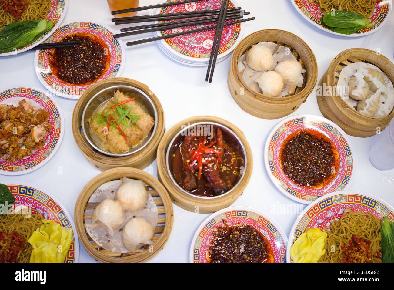 Una festa di dim sum e spaghetti cinesi sparsi su un tavolo bianco, con vari gnocchi al vapore in cesti di bambù, salse piccanti e costolette lunghe Foto Stock
